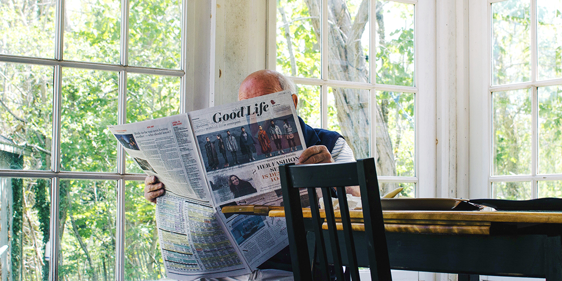 Elderly man reading a newspaper in a sunroom